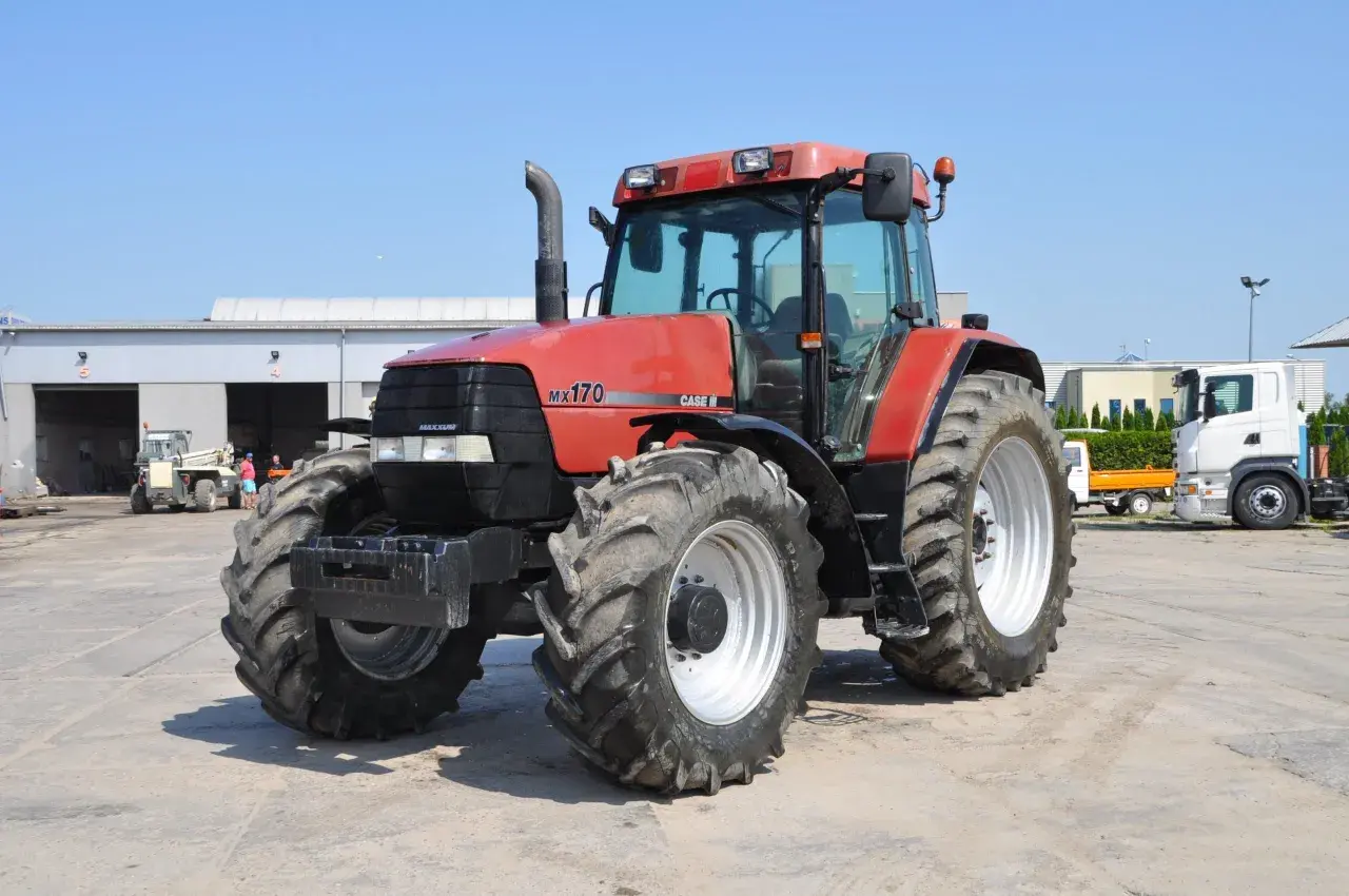 Czerwony traktor Case MX 170 z dużymi oponami stoi na placu. W tle budynki i inne pojazdy.
